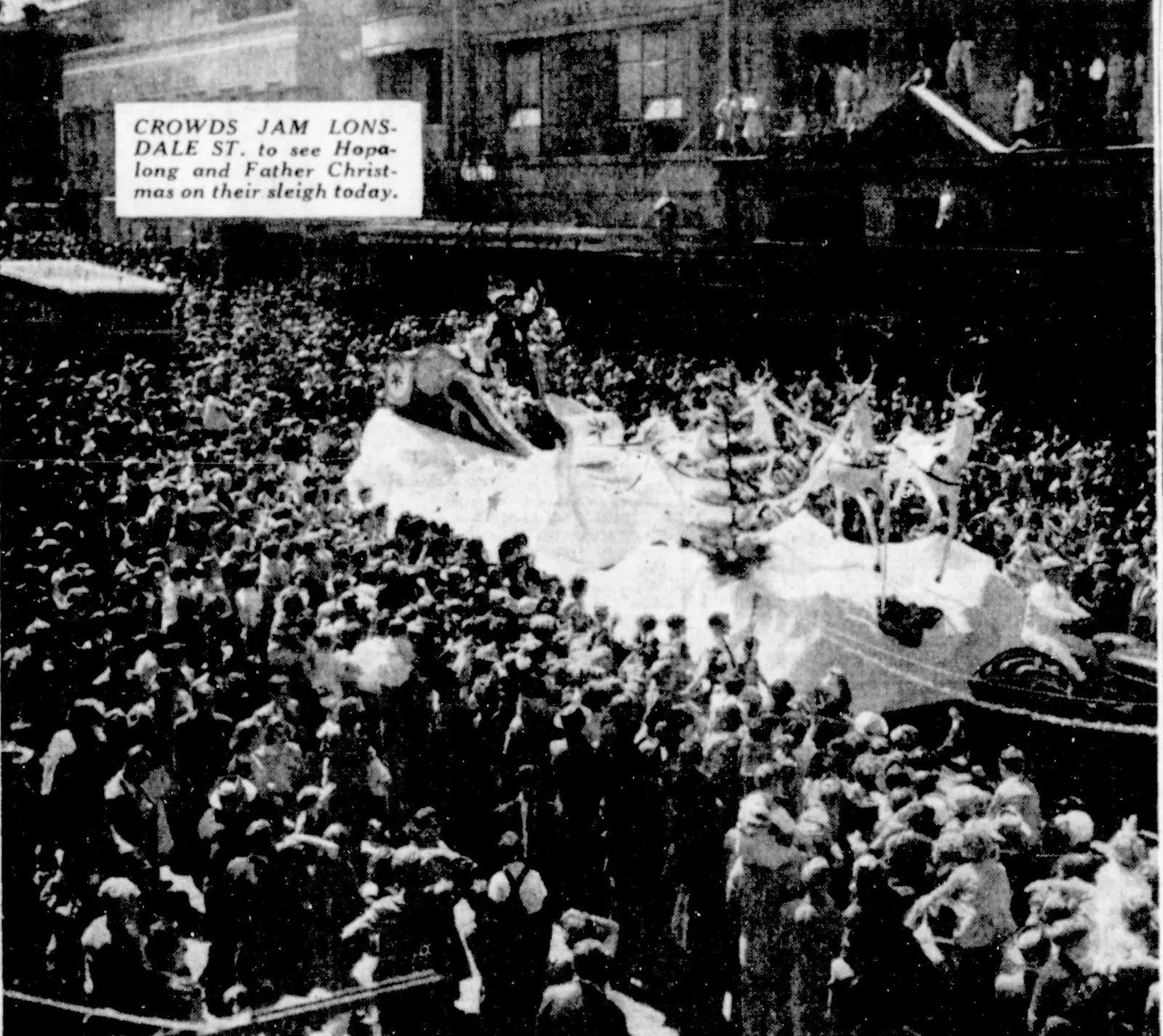 A newspaper photograph from a high window: Lonsdale Street packed from wall to wall, and in the middle of the crowd Father Christmas’s white sleigh float with its reindeer. The inset caption: “Crowds jam Lonsdale St. to see Hopalong and Father Christmas on their sleigh today.”